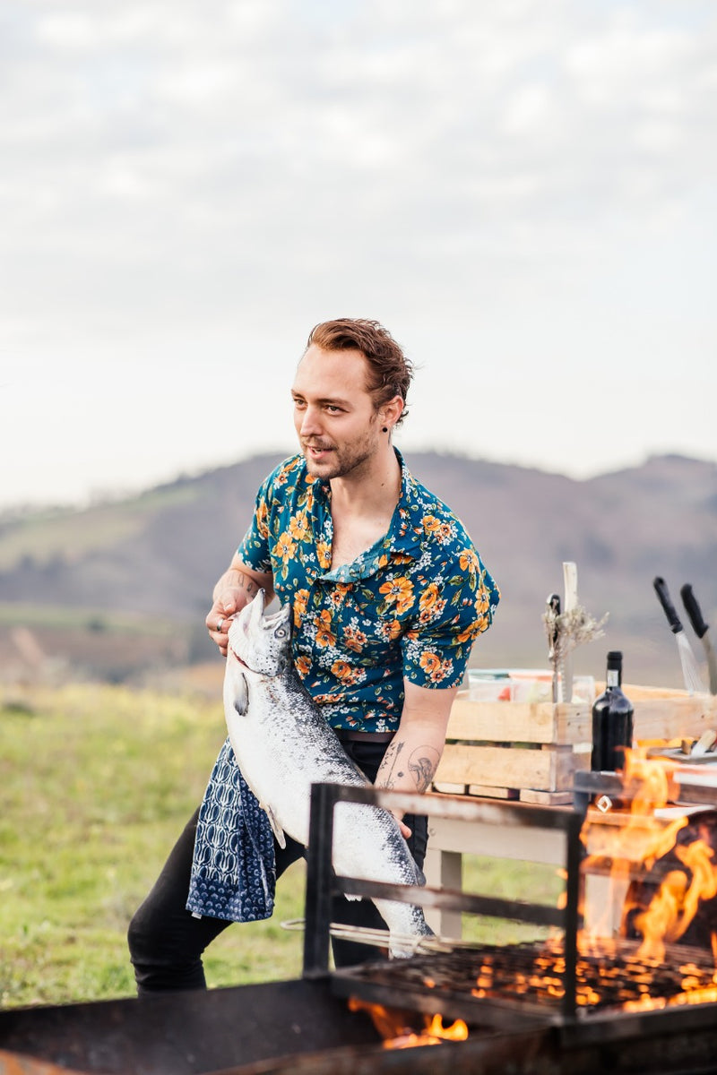 Man cooking outdoors with a grill and mountains in the background