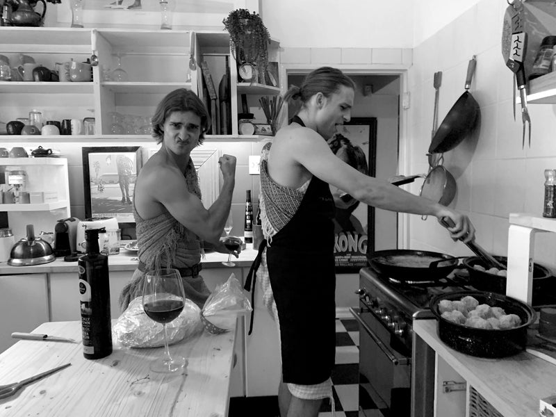 Two people in a kitchen, one cooking on the stove and the other at the counter.
