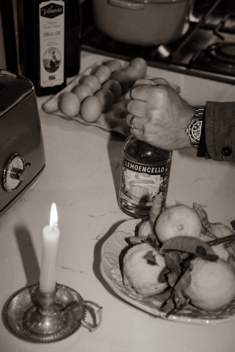 Person holding a bottle of Lemoencello with apples and a lit candle on a table.
