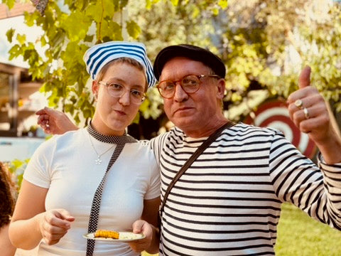 Two people in striped shirts standing outdoors with trees in the background