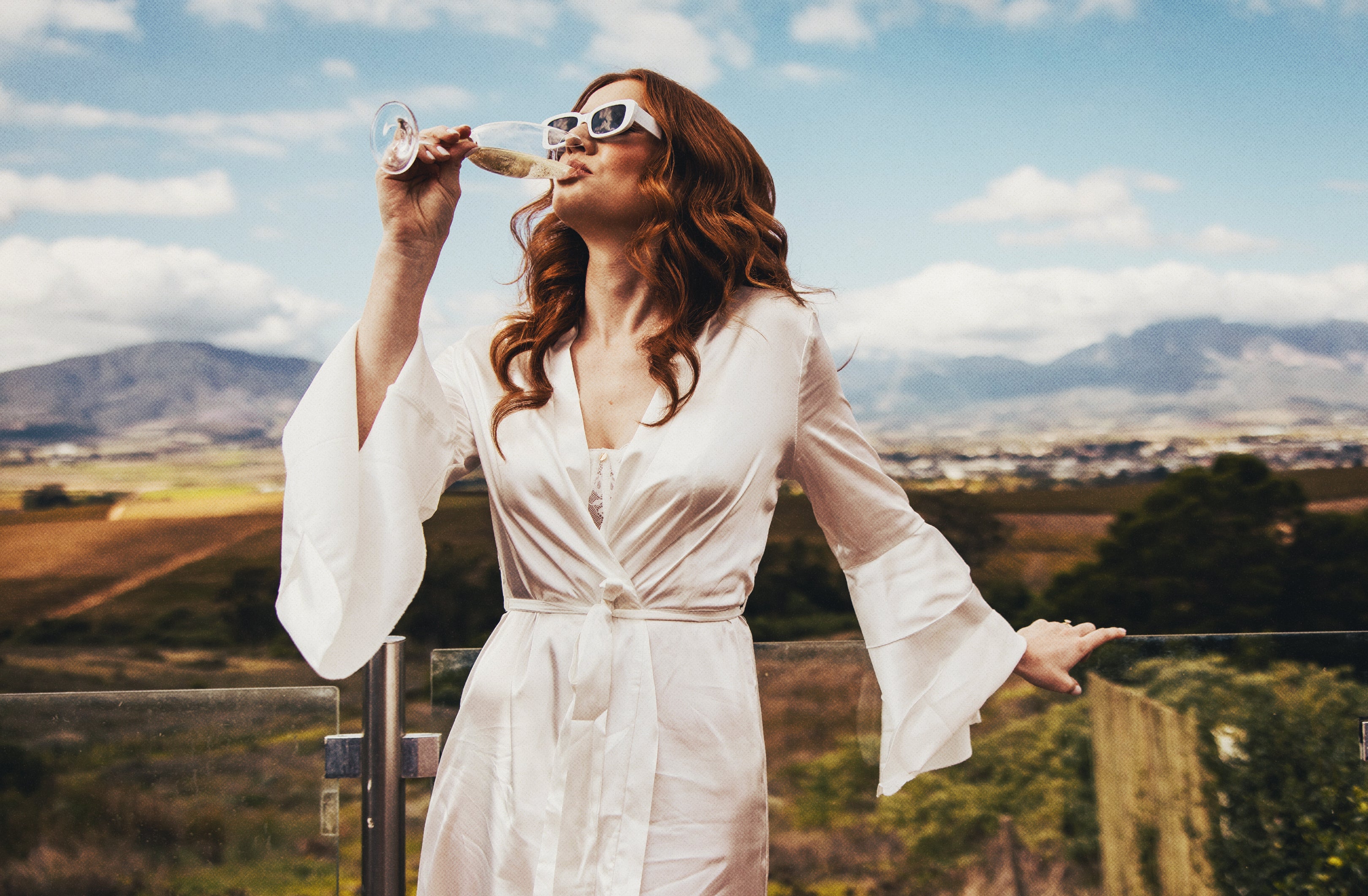 Woman in a white robe enjoying an aperitif with a scenic South African background