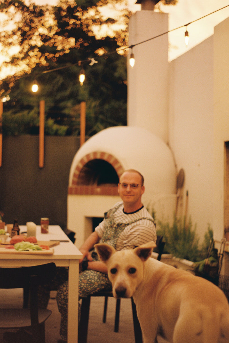 Man sitting at a table with a dog in an outdoor setting
