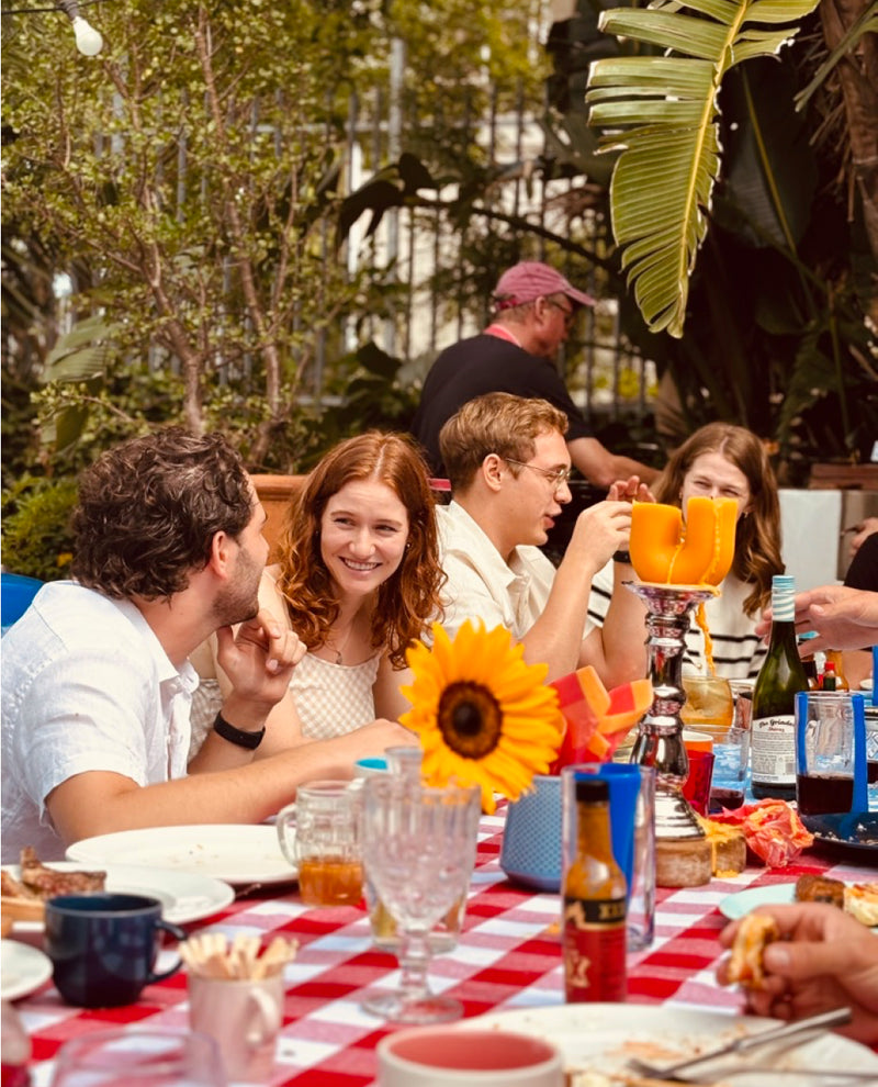 Group of people enjoying a meal outdoors with a red and white checkered tablecloth.