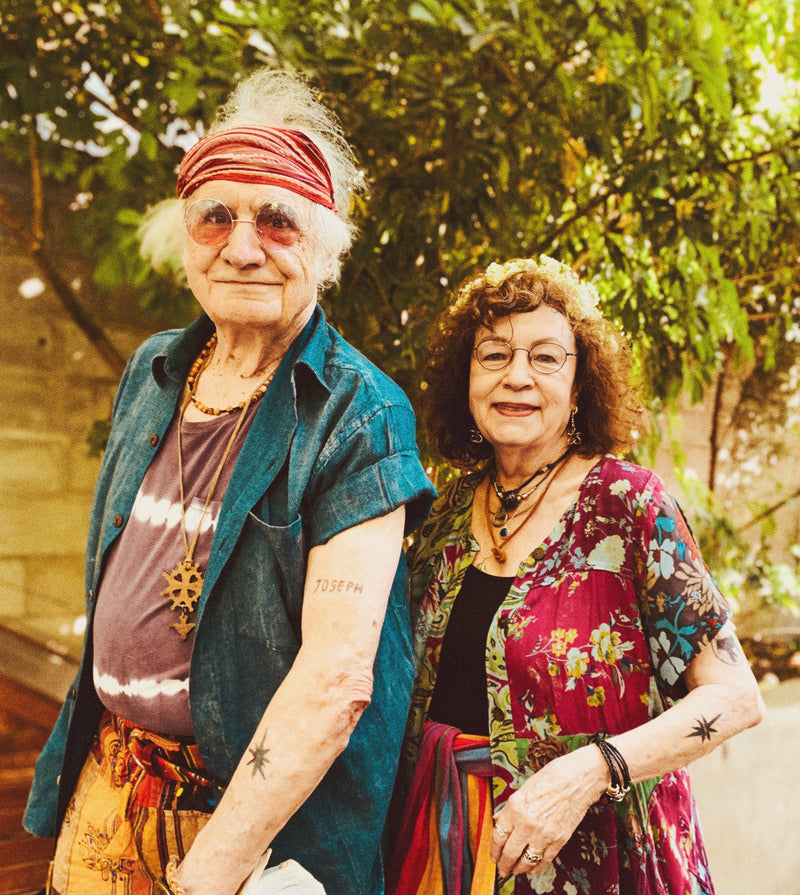 Two people standing in hippy outfits  outdoors with trees in the background